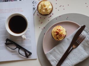 coffee, cup, drink, breakfast, food, chocolate, sweet, table, sugar, espresso, spoon, plate, tea, hot, mug, tea cup, saucer, glasses, desktop, table top, coffee cup, cupcake, cake, icing, dessert, table wear, magazine, read, cafe, caffeine, cappuccino, white, black, beverage, morning