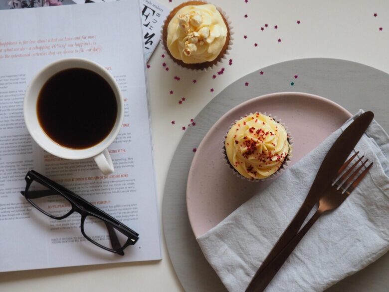 coffee, cup, drink, breakfast, food, chocolate, sweet, table, sugar, espresso, spoon, plate, tea, hot, mug, tea cup, saucer, glasses, desktop, table top, coffee cup, cupcake, cake, icing, dessert, table wear, magazine, read, cafe, caffeine, cappuccino, white, black, beverage, morning